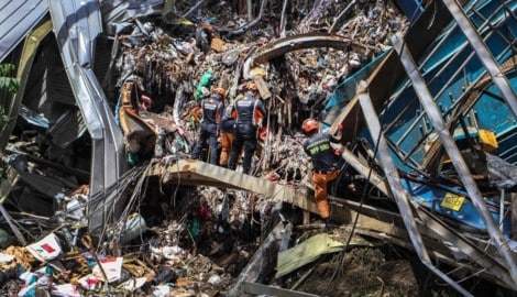 Rettungskräfte mit Schutzhelmen und Bagger suchen in dem Müllberg nach wie vor verzweifelt nach ...