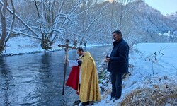 Pfarrer Bernd Wegscheider taucht das Prozessionskreuz in die Glan, Mesner Johann Karner hält ...