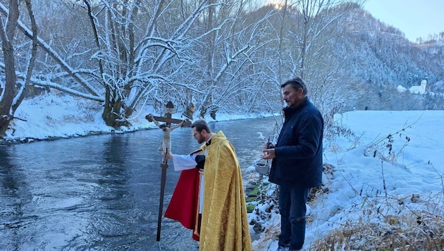 Pfarrer Bernd Wegscheider taucht das Prozessionskreuz in die Glan, Mesner Johann Karner hält ...