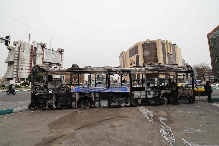 Ein Foto zeigt die Trümmer eines ausgebrannten Busses, auf dem ein Banner mit der Aufschrift ...