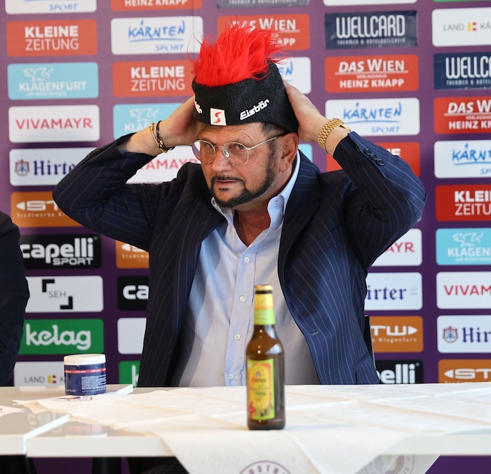 Kaltenegger – mit einer Tube Haargel am Tisch – zieht die Haube bei der PK an.