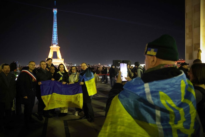 Menschen posieren mit der ukrainischen Flagge vor dem in gelb-blau beleuchteten Eiffelturm.