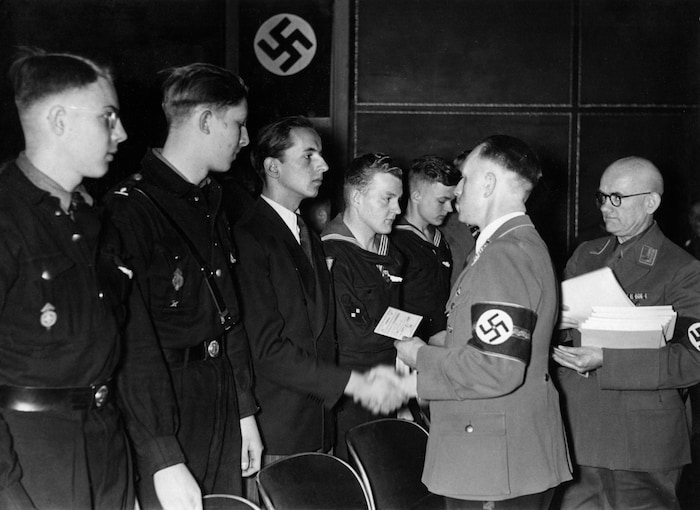 Ein NS-Funktionär überreicht in Berlin Neuzugängen Parteibuch und Parteiabzeichen.