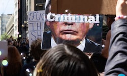 Eine Demonstrantin hält ein Schild hoch, auf dem Donald Trump zu sehen ist. Auf seinem Gesicht ...