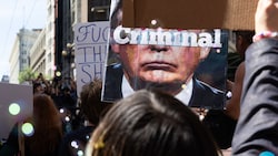 Eine Demonstrantin hält ein Schild hoch, auf dem Donald Trump zu sehen ist. Auf seinem Gesicht ...