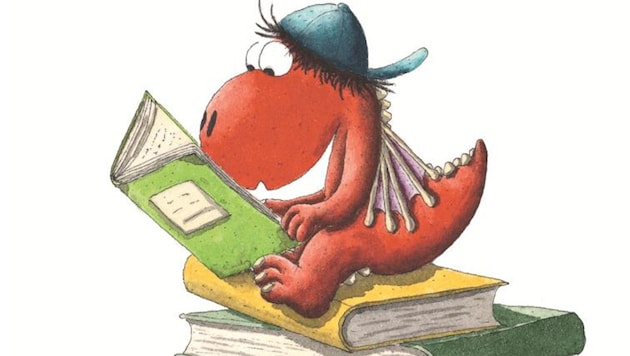 Der kleine Drache Kokosnuss auf einem Bücherstapel