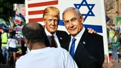 Ein Demonstrant hält eine Zeichnung von Trump und Netanyahu in die Höhe.