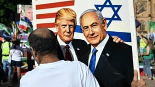 Ein Demonstrant hält eine Zeichnung von Trump und Netanyahu in die Höhe.