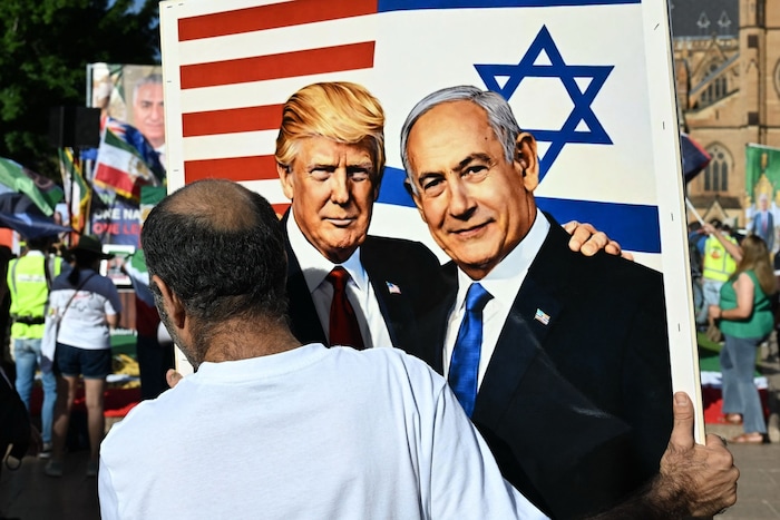 Ein Demonstrant hält eine Zeichnung von Trump und Netanyahu in die Höhe.