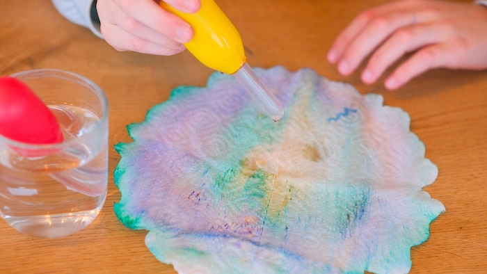 Mithilfe einer Pipette werden vorsichtig Wassertropfen am Papier verteilt, bis die Farben sanft ...