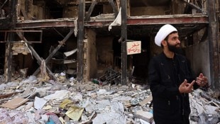 Ein iranischer Geistlicher neben beschädigten Wohngebäuden (Archivbild)