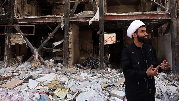Ein iranischer Geistlicher neben beschädigten Wohngebäuden (Archivbild)