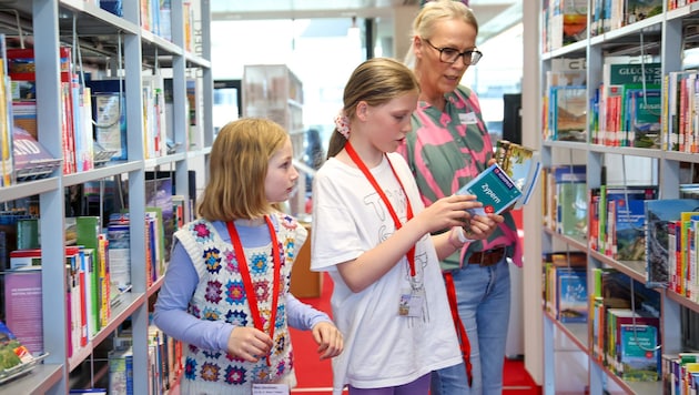 Lovis (10) und Josefine (10; re.) mit Mitarbeiterin Christine sortieren Reiseführer ins Regal.