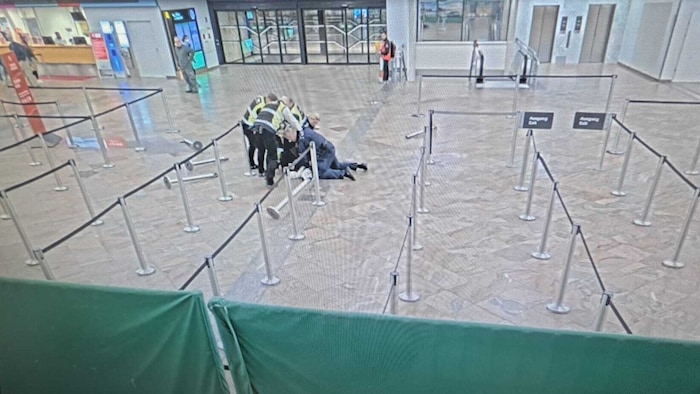 Polizisten und private Flughafen-Securitys liegen auf dem lettischen 100-Kilo-Mann, um ihn zu ...