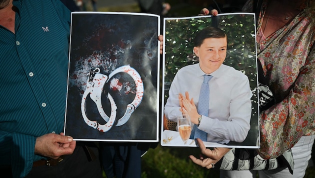 Menschen halten Bilder des Opfers Henry Nowak und blutverschmierte Handschellen in den Händen, ...
