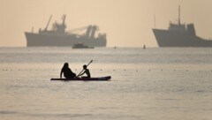 Eine iranische Frau und ihr Sohn beim Paddleboarding an vorbeifahrenden Schiffen, die in der ...
