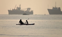 Eine iranische Frau und ihr Sohn beim Paddleboarding an vorbeifahrenden Schiffen, die in der ...