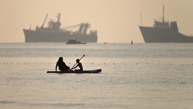 Eine iranische Frau und ihr Sohn beim Paddleboarding an vorbeifahrenden Schiffen, die in der ...