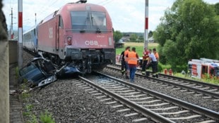 Das zerstörte Auto mit Zug und Einsatzkräfte auf den Bahngleisen