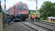 Das zerstörte Auto mit Zug und Einsatzkräfte auf den Bahngleisen