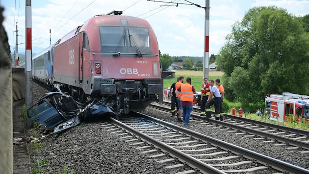 Das zerstörte Auto mit Zug und Einsatzkräfte auf den Bahngleisen