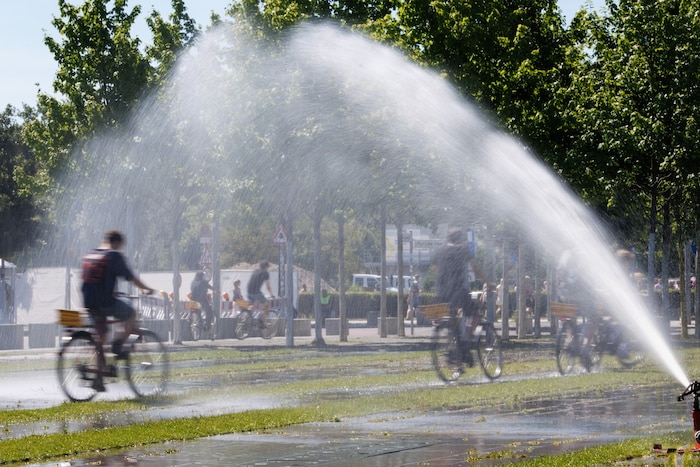 Fahrradfahrer in Berlin erfrischen sich bei einem Sprinkler.