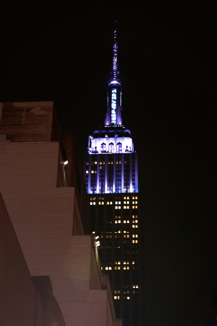 Das Empire State Building in Lavendeltönen, während Tausende Fans vor der Arena auf einen Blick ...