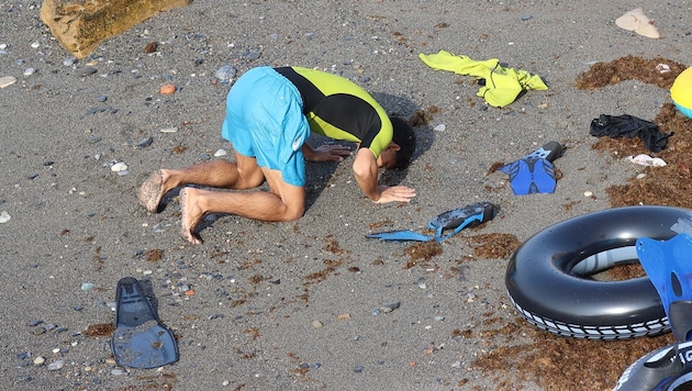 A man says a prayer upon his arrival. Dozens of migrants did not make it out of the water.