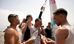 Junge Migranten versorgen sich aus einer Dusche am Strand mit frischem Wasser.