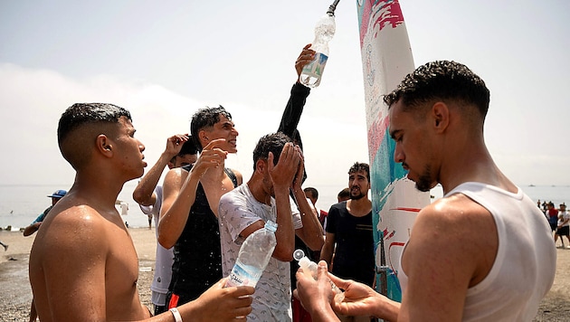 Young migrants get fresh water from a shower on the beach.