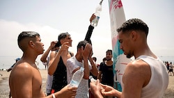 Junge Migranten versorgen sich aus einer Dusche am Strand mit frischem Wasser.