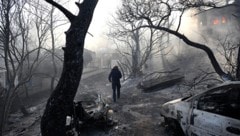 Ein Feuerwehrmann geht durch ein verbranntes Gebiet, während Flammen ein Haus auf der Insel ...