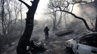 Ein Feuerwehrmann geht durch ein verbranntes Gebiet, während Flammen ein Haus auf der Insel ...