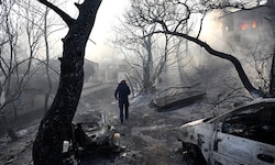 Ein Feuerwehrmann geht durch ein verbranntes Gebiet, während Flammen ein Haus auf der Insel ...
