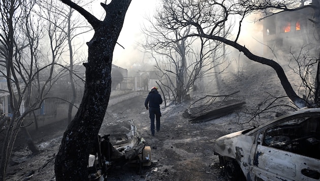 Ein Feuerwehrmann geht durch ein verbranntes Gebiet, während Flammen ein Haus auf der Insel ...