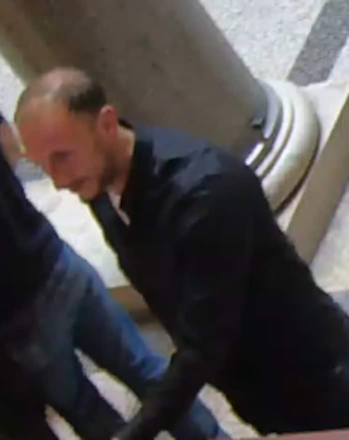 ... dunkle Haare, dunkler Bart schwarze Oberbekleidung sowie dunkle Turnschuhe mit weißer Sohle.