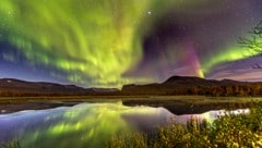 In einer kalten Septembernacht tanzen die Nordlichter über einem kleinen See nahe Nikkaluokta, ...