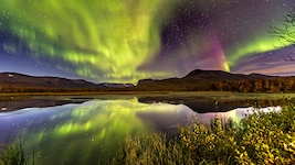 In einer kalten Septembernacht tanzen die Nordlichter über einem kleinen See nahe Nikkaluokta, ...