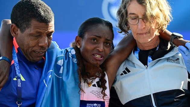 Tigst Assefa (M.) muss nach ihrem Sieg beim Berlin-Marathon von Helfern gestützt werden …