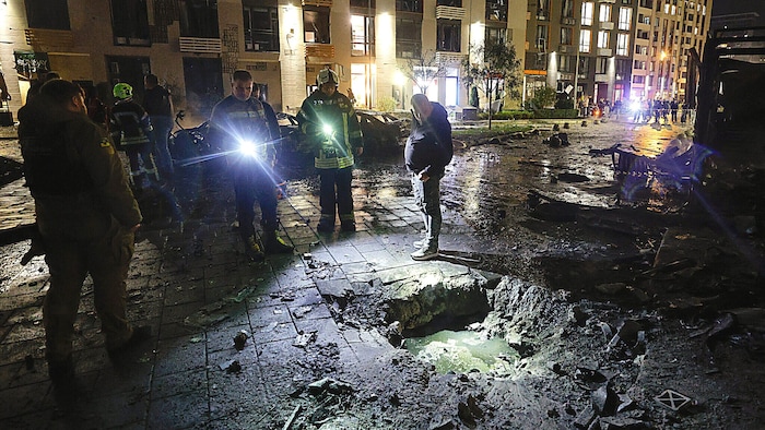 Einsatzkräfte und Passanten inspizieren Schäden nach einem Drohnenangriff auf ein Wohnviertel ...