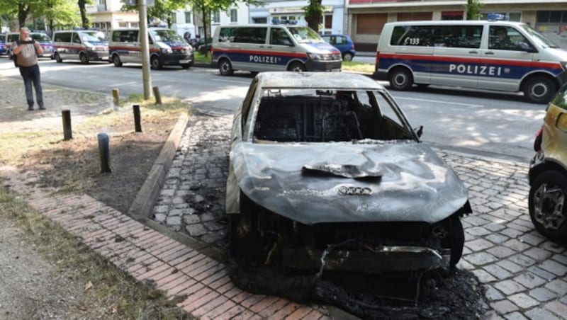 Ein ausgebranntes Auto, im Hintergrund Einsatzfahrzeuge der österreichischen Polizei (Bild: AFP)