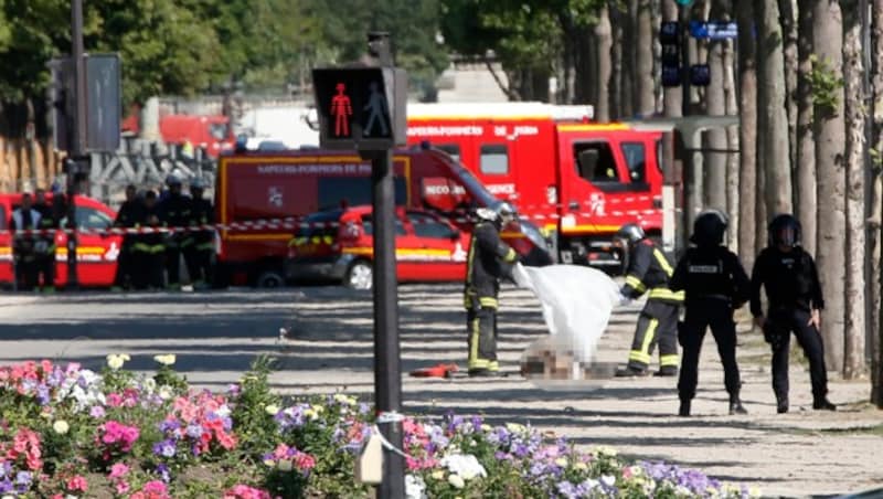 Einsatzkräfte breiten ein Leichentuch über den regungslos am Boden liegenden Mann. (Bild: AP)