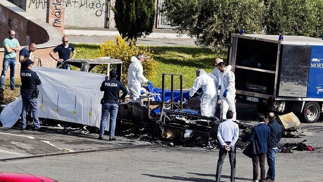 Tatortermittler inspizieren die Überreste des total ausgebrannten Wohnmobils. (Bild: AP/ANSA/Massimo Percossi)