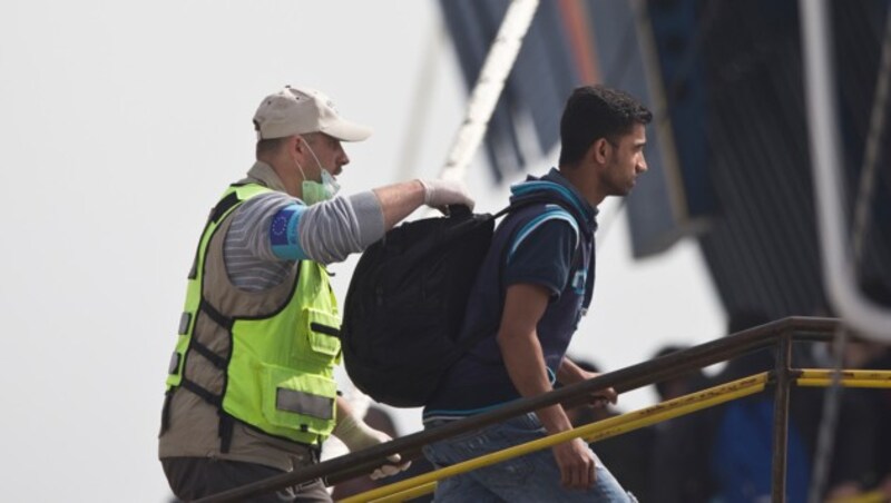 Ein Frontex-Beamter begleitet einen Flüchtling an Bord einer Fähre. (Bild: ASSOCIATED PRESS)