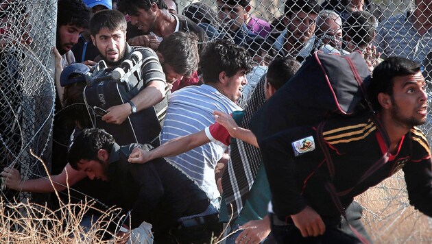 Flüchtlinge durchbrechen einen Grenzzaun zwischen Syrien und der Türkei. (Bild: AP)