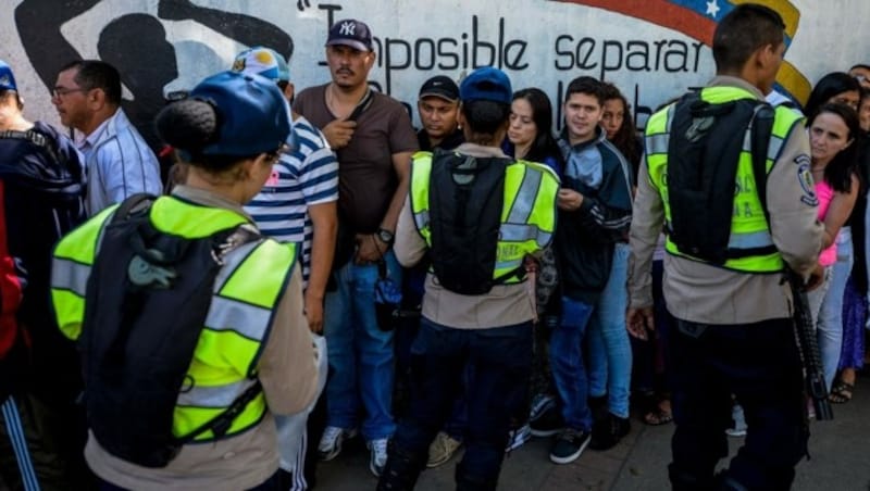 Polizisten überwachen Menschen, die vor einem Lebensmittelgeschäft in Caracas Schlange stehen. (Bild: APA/AFP/FEDERICO PARRA)