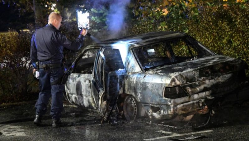 Ein Polizist vor einem ausgebranntem Auto (Bild: AP)