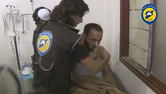 Ein Mann in Atemnot bekommt von einem Helfer eine Atemschutzmaske gereicht. (Bild: Screenshot/Zoomin.TV)