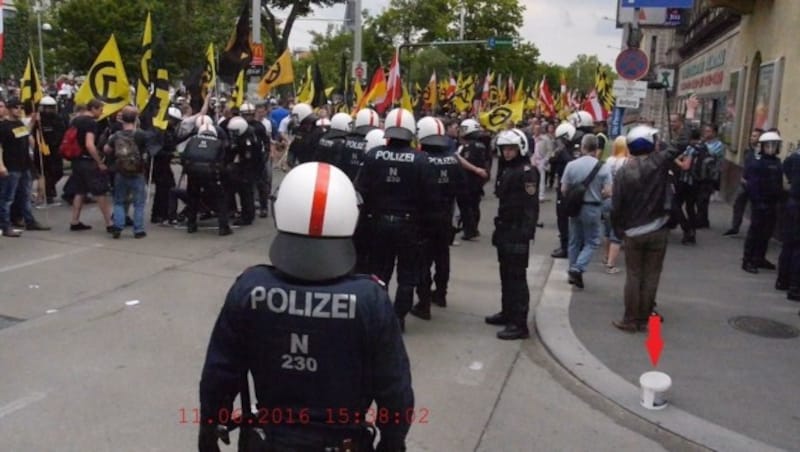 Dieses Polizeibild zeigt den Tatort kurz nach dem Steinwurf und den geworfenen Kübel (Pfeil). (Bild: LPD Wien)