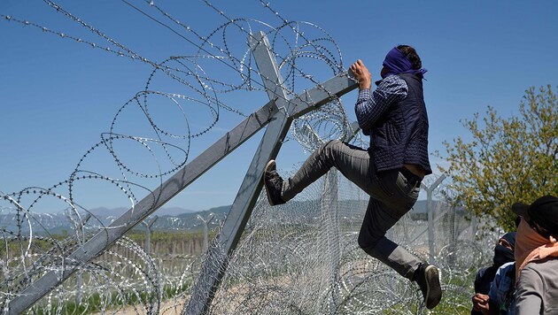 16.4.: Ein vermummter Migrant versucht den Grenzzaun zu Mazedonien zu überwinden. (Bild: APA/AFP/Daniel Mihailescu)